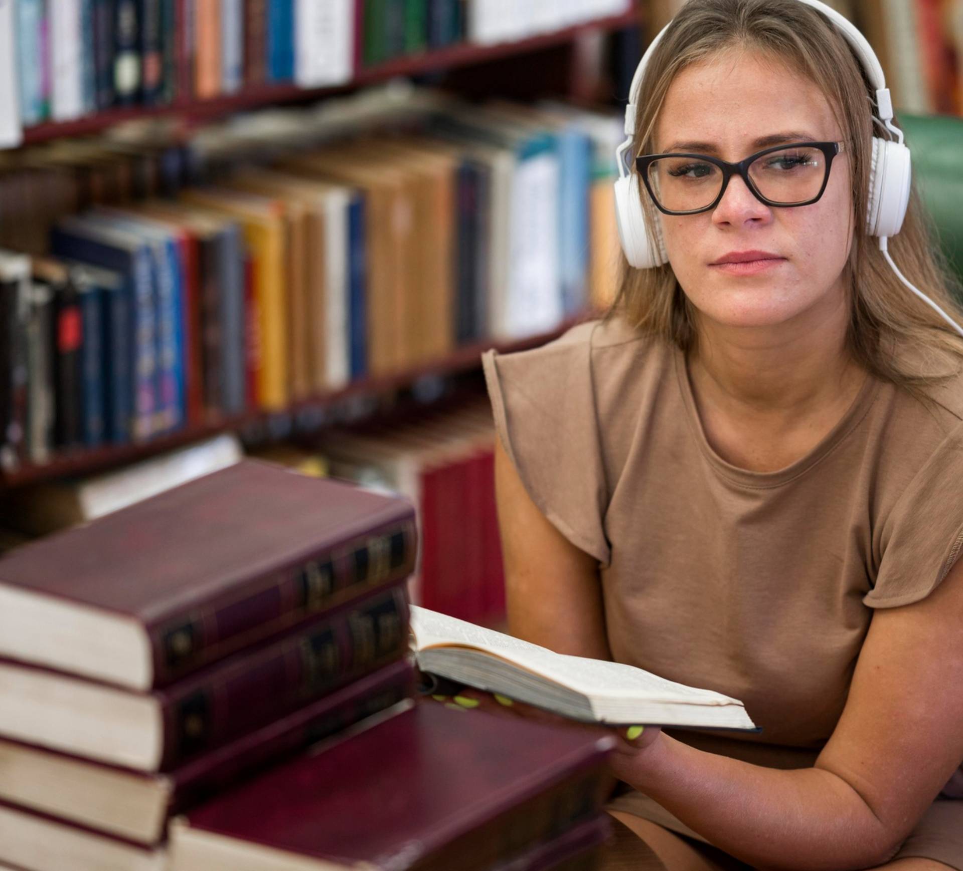 Person with headphones reading a book in a library.